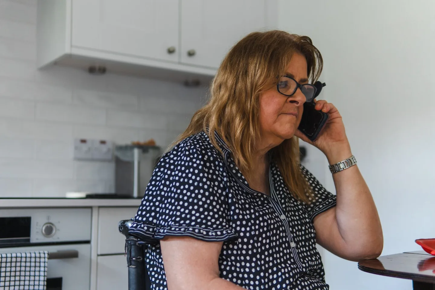 A woman taking a phone call in her kitchen in the evening